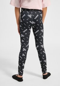 Svarta leggings med ett upprepat vitt logomönster, tillverkade av elastiskt material, med en figursydd design och en medelhög midja.