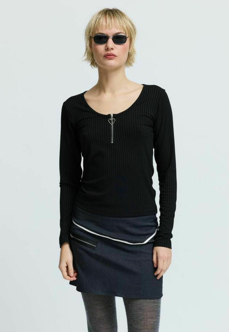 Čierne rebrované tričko s dlhým rukávom, okrúhlym výstrihom a zipsom v tvare srdca. Doplnok tvorí tmavá denimová sukňa s ozdobným pásikom a predným vreckom.