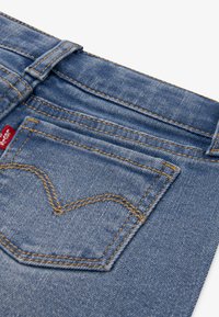 Blå denimjeans med hög midja, med en rektangulär bakficka och karakteristisk orange sömnad i hjärtform.