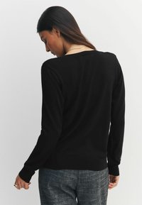 Pulover negru cu mâneci lungi, croială lejeră, textură moale și manșete ribbed. Prezintă un decolteu larg și un design casual pe spate.