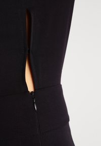 Svart figursydd klänning med en sidoklyfta och en dold dragkedja i midjan, gjord av texturerad tyg, som visar upp rena linjer och struktur.