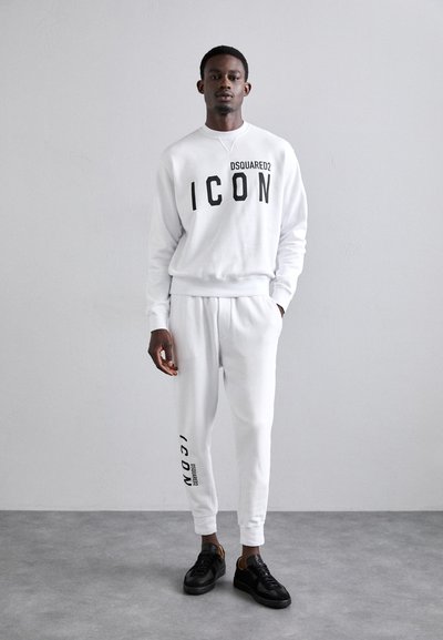 White sweatshirt and matching joggers with black "ICON" text. Material appears soft. Black shoes with yellow accents. Simple, modern design.