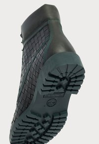 Black and teal high-top boot with woven upper, rubber sole featuring textured treads and a green accent along the seams.
