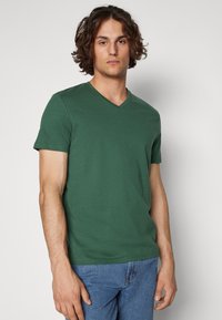 Green cotton t-shirt with a v-neck and short sleeves, featuring a solid color and a classic fit, paired with blue denim jeans.