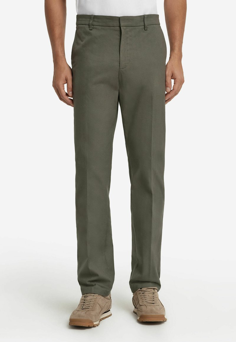 Olivgrüne, maßgeschneiderte Hose mit glatter Textur, geradem Bein, Gürtelschlaufen und Seitentaschen, kombiniert mit beigen Sneakers.