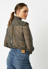 Brown and black striped blouse with ruffled collar, sheer fabric, and long sleeves, paired with high-waisted blue jeans featuring a logo patch.