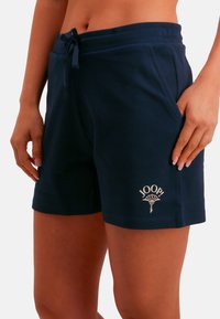 Pantalones cortos de algodón azul marino con cintura elástica, cordón ajustable, bolsillos laterales y un pequeño diseño de logo blanco en la pierna izquierda.