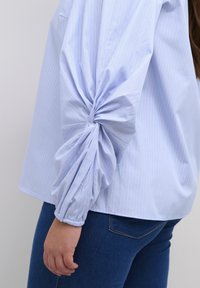 Lichtblauw gestreepte blouse met volumineuze, gedraaide mouwen en gathered manchetten, gecombineerd met donkerblauwe jeans. Glad materiaalsamenstelling.