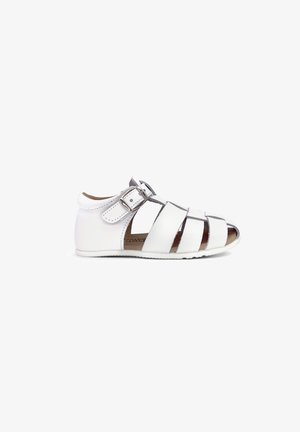 Hvid læderbaby sandal med lukket hæl, åben tå, flere stropper og en sølv spænde på hvid baggrund.