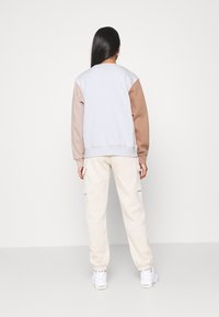 Felpa grigia chiara con maniche marroni, polsini a coste e una vestibilità rilassata, abbinata a pantaloni jogger beige con tasche laterali.