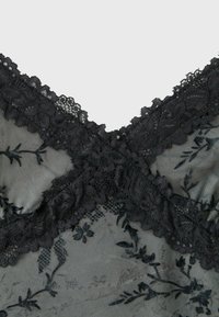 Black lace fabric with floral embroidery and scalloped edges arranged in an X shape on a sheer mesh background.
