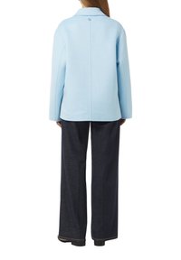 Giacca in misto lana di colore azzurro chiaro con colletto, dettaglio a singolo bottone al collo, abbinata a pantaloni in denim largo di colore scuro. Vista posteriore.