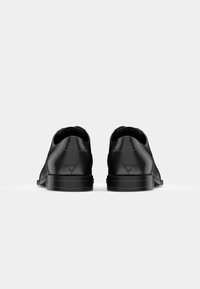Black leather shoes seen from the back. Sleek design with a smooth texture, rounded toe, and low-profile rubber sole.