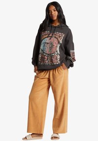 Sudadera negra de gran tamaño con un gráfico de esqueleto colorido, combinada con pantalones de pana beige de pierna ancha y sandalias blancas tipo slider.