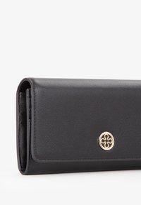 Portafoglio in pelle nera con una texture liscia, forma rettangolare e un logo circolare color oro sul davanti.