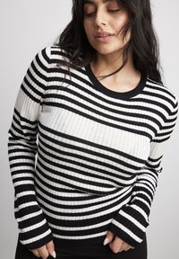 Black and white striped ribbed long-sleeve sweater with a round neckline and fitted cuffs, showcasing a textured knit design.