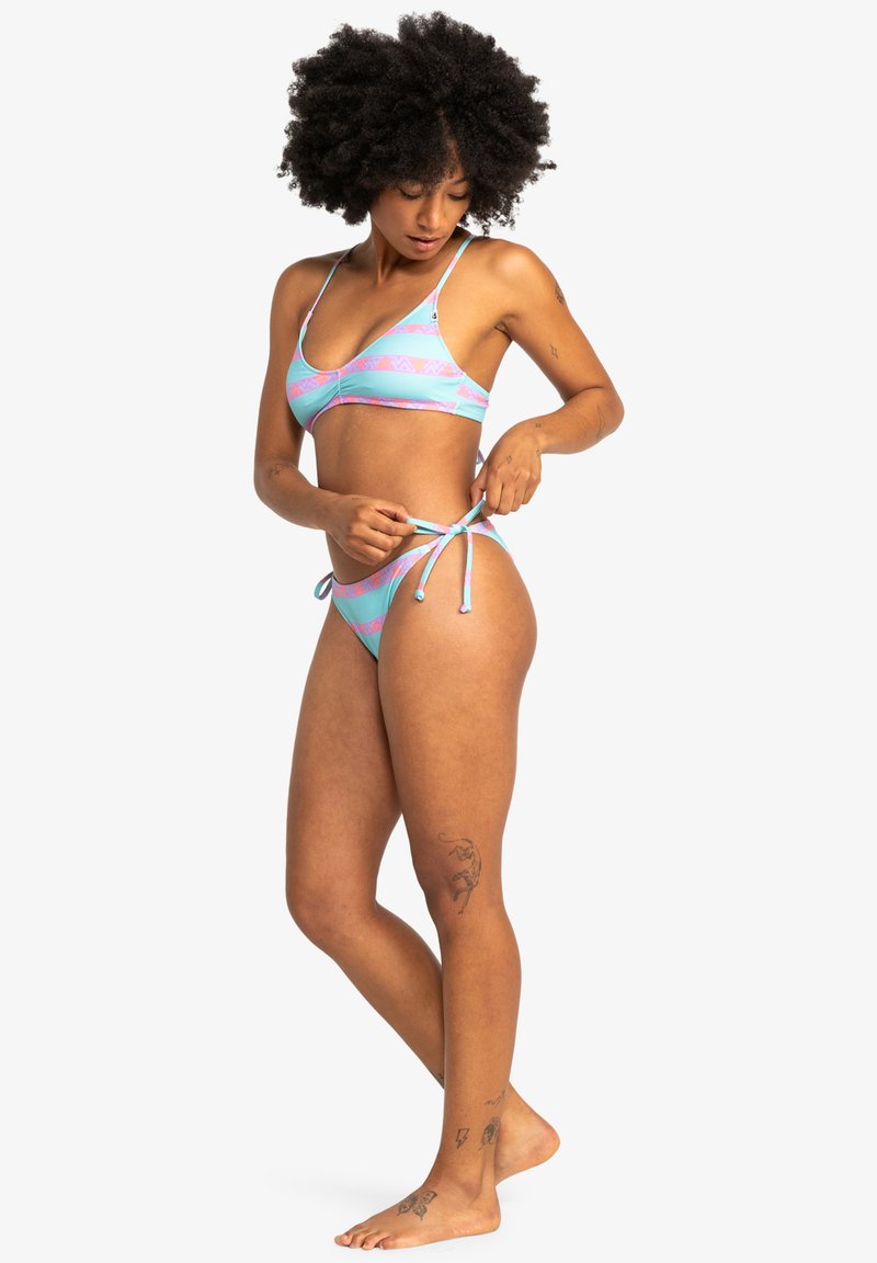 Bikini set s světle modrým základem a růžovými geometrickými vzory, nastavitelné šňůrky po stranách a jemnou texturou.