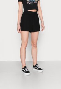 Black, high-waisted shorts with a flowing design, featuring a textured fabric. Paired with black and white sneakers.