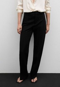 Pantalon noir ajusté avec une coupe droite, taille haute et texture lisse, assorti à un chemisier léger boutonné.