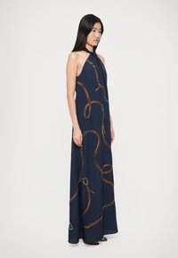 Rochie maxi bleumarin cu decolteu halter, cu modele aurii și maro asemănătoare unor lanțuri, material neted, croială lejeră, lungime până la gleznă, cu un detaliu de decolteu cu decupaj în formă de cheie.