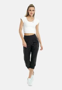 Vit kortärmad cropped skjorta i kombination med svarta, tapered byxor i ankellängd som har fickor och elastiska nederkanter. Vita sneakers.