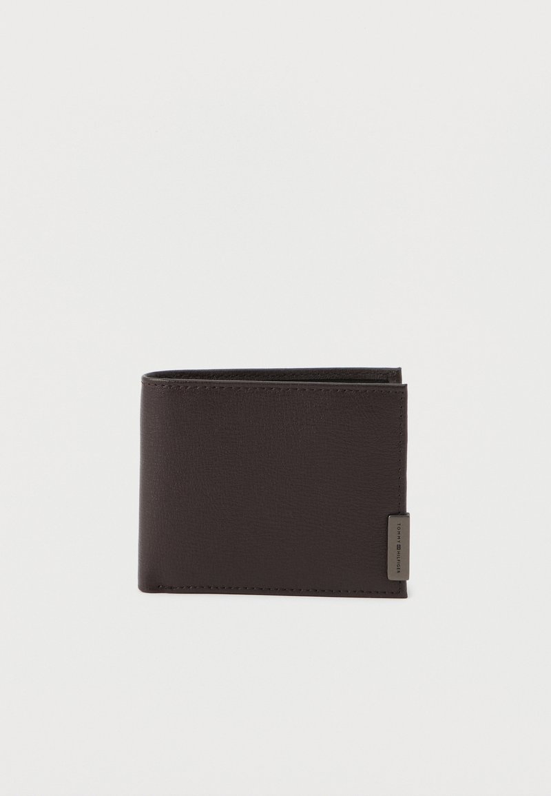 Tmavohnedrá kožená bifold peňaženka s malou kovovou štítkom v dolnom pravom rohu, umiestnená na bielom pozadí.