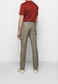 Pánské červené tričko s krátkým rukávem v kombinaci se světlými béžovými kalhotami rovného střihu a krémovými teniskami, zobrazené zezadu.