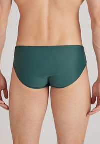 Grüne Schwimmbrieftaschen aus leichtem, dehnbarem Material. Sie verfügen über einen niedrigen Schnitt und nahtlose Kanten für einen glatten Sitz.