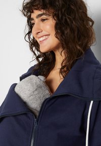 Giacca a zip blu navy con colletto alto, dotata di un morbido rivestimento in tessuto grigio per garantire calore. Ha una tasca per trasportare oggetti o un bambino.