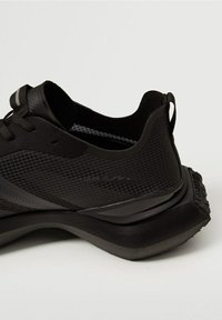 Chaussures de sport noires avec une tige en mesh texturé, une semelle en caoutchouc et un talon rembourré. Présentent un motif en grille subtil et des accents réfléchissants.