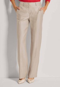 Beige op maat gemaakte broek met een rechte pijpdesign, voorzien van voorkruisplooien en zijzakken, gecombineerd met lichtgekleurde schoenen.