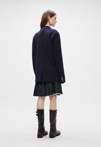 Ναυτικό σακάκι, δομημένος σχεδιασμός, κλείσιμο με ένα κουμπί, σε συνδυασμό με πράσινη καρό φούστα και μαύρες μπότες μέχρι το γόνατο με τόνους από αγκράφες.