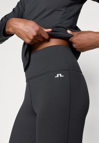 Leggings deportivos negros con una cinturilla ancha, textura suave y un acento de logo blanco en la cadera. Un diseño ajustado y minimalista.