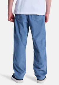 Pantalons larges en velours côtelé bleu clair avec une texture côtelée. Comprend deux poches arrière et une coupe décontractée, associés à des baskets navy.