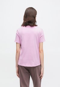 Keskmise pikkusega pruunide juustega inimene seisab seljaga vastu, kandes helesinist lühikeste varrukatega särk ja pruune pükse.