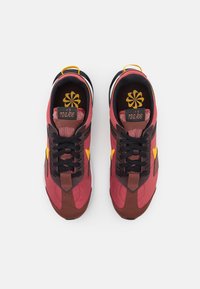 Tenisky Nike s burgundy a hnědými textiliemi, černými tkaničkami, žlutými akcenty a vzorovanou stélkou s logem značky.