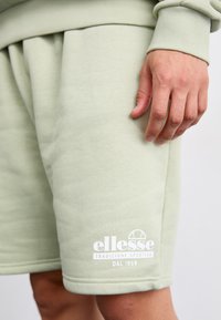 Svetlozelené bavlnené šortky s elastickým pásom, bočnými vreckami a bielym logom s detailom "ellesse tradizione sportiva DAL 1959".