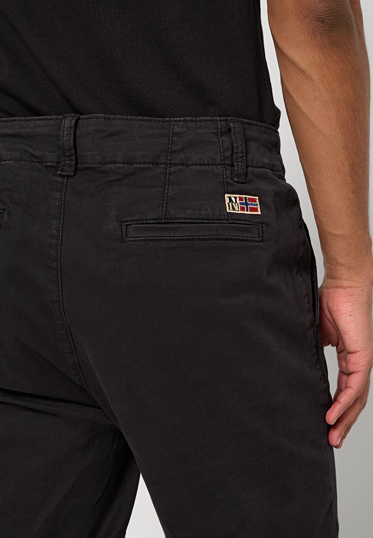 Schwarze Baumwollhose mit einer Gesäßtasche, die mit einem kleinen gestickten norwegischen Flaggenpatch verziert ist. Der Stoff wirkt glatt mit einem geraden Schnitt.