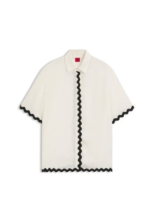 Blusa blanca de manga corta con ribete ondulado negro a lo largo de la línea de botones, bordes de las mangas y dobladillo, con cuello clásico y etiqueta interior roja.