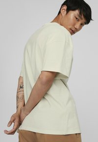 Lys grøn bomulds t-shirt med korte ærmer, afslappet pasform og rund halsudskæring, vist fra en svag vinkel med en neutral baggrund.