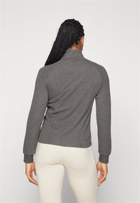 Hallgrey pikkade varrukatega särk kõrge kraega, kitsas lõige, pehme tekstuur ja soonikvarrukad. Kanna heledate pükstega. Minimalistlik disain.