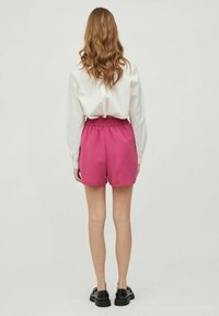 Růžové šortky s elastickým pasem, vyrobené z texturované látky. Kombinované s bílou košilí s dlouhým rukávem a černými botami.