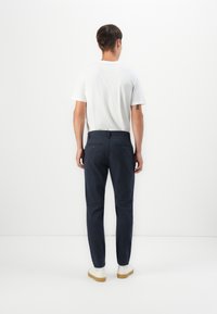 Pantalones de marina con corte ajustado, que cuentan con dos bolsillos traseros y una textura suave, combinados con una camiseta blanca simple y zapatillas ligeras.