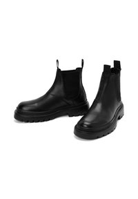 Par de botas Chelsea de cuero negro con paneles laterales elásticos y suelas de goma gruesa, mostradas sobre fondo blanco.