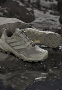 Light beige Adidas Terrex hiking shoes with Gore-Tex and Continental rubber soles resting on wet rocky ground.