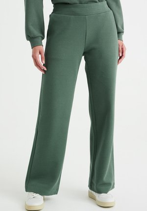 Green textured wide-leg pants worn with white sneakers, shown on a standing person from waist to feet against a plain background.