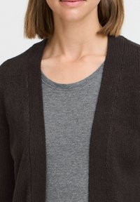 Dark brown knitted cardigan with an open front design, featuring a textured fabric. Worn over a light gray t-shirt with a round neckline.