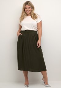 Olive green midi skirt with elastic waistband, pockets, paired with a white t-shirt. Model wears silver heeled shoes.