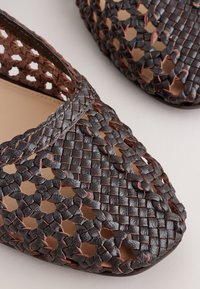 Close-up of dark brown woven leather shoes with braided and interlaced pattern revealing beige inner lining.
