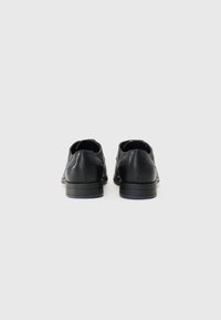 Zapatos de cuero negro con un acabado suave, punta redondeada y tacón bajo, que cuentan con detalles de costura sutil en la parte trasera.
